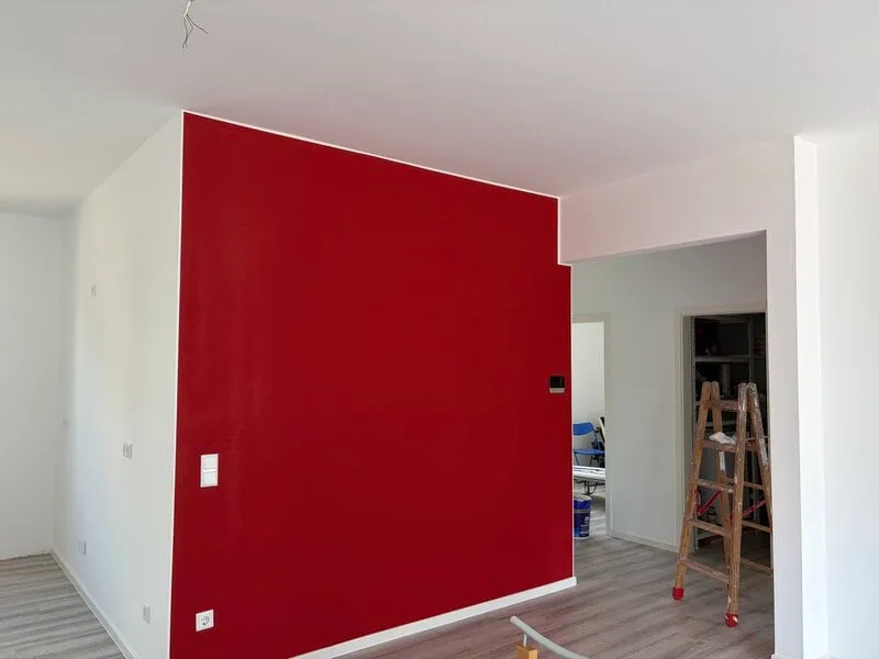 Renovierter Wohnraum mit kräftig roter Akzentwand und weißen Wänden