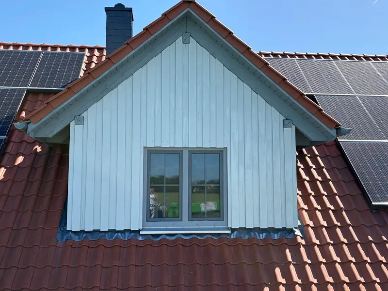 Dachgaube mit weiß gestrichener Holzverschalung zwischen roten Dachziegeln